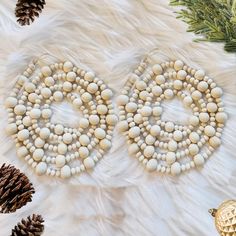 a pair of white beaded earrings sitting on top of a fur covered floor next to pine cones