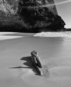 a woman laying on top of a sandy beach next to the ocean