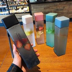 a person holding an item in front of four different colored containers on a wooden table