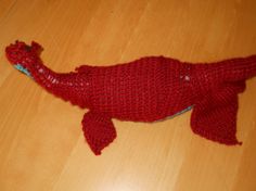 a red knitted alligator laying on top of a wooden floor