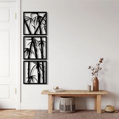 a wooden table sitting in front of a white wall with three black paintings on it