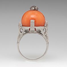 This fabulous antique circa 1930s ring is centered with one (1) round coral bead topped with a cluster setting accented with five (5), bezel set, old mine cut diamonds. The top half of the ring features engraved details and bordered with milgrain edging. The shoulders of the ring are each accented with three (3), bead set, old European cut diamonds. The ring measures 16.8mm at the top, rises 17.2mm above the finger, tapering to 1.4mm wide and 1.3mm thick at the base of the shank. Trademarks: Noble & Co. It is crafted in platinum and is currently a size 6.5. Vintage Diamond Cabochon Rings, Vintage Diamond Rings With Cabochon, Art Deco Carved Round Jewelry, Antique Round Orange Jewelry, Antique Orange Round Jewelry, Vintage Orange Rings For Formal Occasions, Vintage Orange Rings For Collectors, Orange Vintage Rings For Formal Occasions, Vintage Orange Cabochon Rings