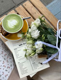 there is a cup of green tea next to some flowers and a menu on a table