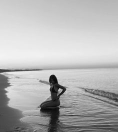 a woman sitting on top of a surfboard in the ocean next to a beach