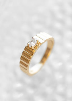 a yellow gold ring with a single diamond on it's side, against a white background