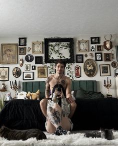 a man sitting on top of a bed next to a black couch covered in pictures