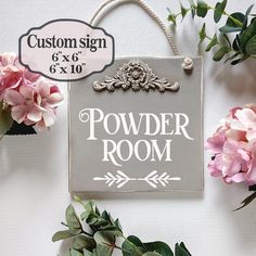 a sign that says powder room next to some pink flowers and greenery on a white wall