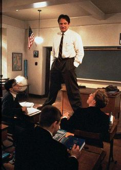 a man standing on top of a desk in a classroom