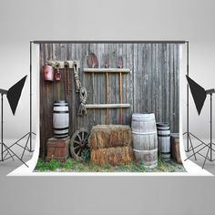 an old barn with hay bales, barrels and other items in front of it