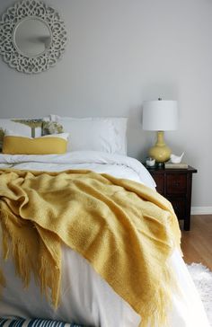 a bed with yellow blankets and pillows in a bedroom next to a mirror on the wall