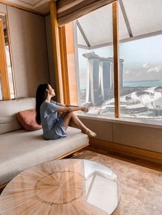 a woman sitting on top of a couch looking out a window at the city below