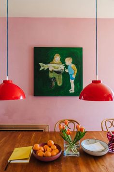 a painting hangs on the wall above a dining room table with oranges and bowls of fruit