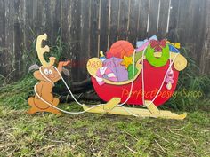 a wooden sleigh with cartoon characters on it sitting in the grass next to a fence