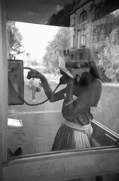 a woman is talking on her cell phone while standing in front of a bus window