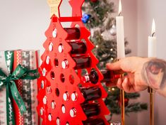 a person holding a wine bottle in front of a christmas tree with candles on it