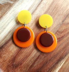 Introducing these fabulous retro drop earrings! Inspired by Pop Art designs from the 1960s, these circle drop earrings are sure to make a statement. Handmade in brown, orange and yellow resin, these colour block earrings are crafted to create a sleek and modern look. The geometric design adds a touch of sophistication, while the bold design adds a pop of contrast. Perfect for any occasion, these unique earrings are a must-have accessory for those who love to embrace retro vibes with a modern twi Retro Round Earrings For Party, Retro Yellow Dangle Jewelry, Retro Party Earrings, Retro Handmade Orange Earrings, Retro Yellow Dangle Earrings, Handmade Retro Orange Earrings, Retro Orange Jewelry For Party, Handmade Vintage Circle Earrings, Retro Handmade Drop Earrings