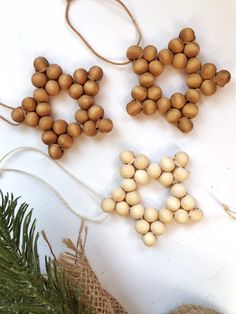 three wooden beads are hanging from twine strings on a white surface next to pine cones