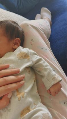 a woman holding a baby in her arms while laying on a bed with blue sheets