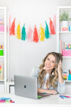 a woman sitting at a desk with a laptop in front of her and colorful streamers on the wall behind her