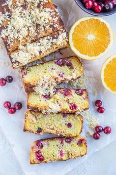 slices of cranberry orange bread on parchment paper next to sliced oranges and cranberries