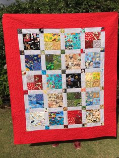 a red and white quilt is hanging on a clothes line in front of some bushes