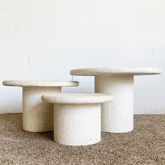 three white concrete tables sitting on top of a carpeted floor next to a wall