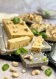 several pieces of cheese and nuts on a cutting board next to a knife with some leaves