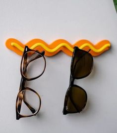 two pairs of glasses sitting next to each other on a white surface with an orange and yellow wave behind them