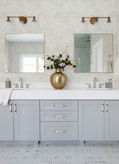 a bathroom with two sinks, mirrors and gold vase filled with flowers on the counter