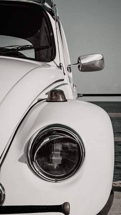 the front end of an old white car parked by the water with its hood up