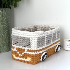 a crocheted basket with a bus design on the front and sides, next to a potted plant