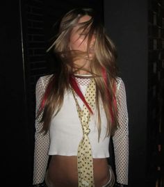 a woman with long hair wearing a white shirt and yellow tie, standing in front of a black wall