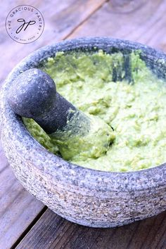 a mortar bowl filled with guacamole on top of a wooden table