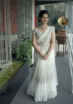 a woman in a white sari standing next to a wall with beads on it