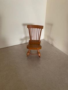 a small wooden chair sitting on top of a gray floor next to a white wall