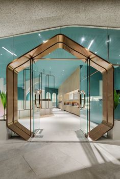 the entrance to an office building with glass walls and gold accents on the doors, along with potted plants