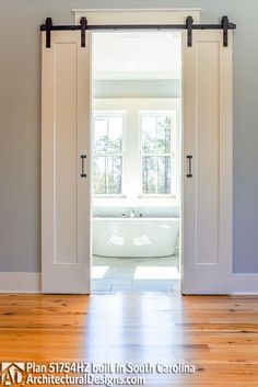 an open door leading to a bathroom with a tub in the corner and wooden floors