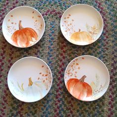 four plates with painted pumpkins on them sitting on a carpeted surface in front of a rug