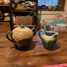 two ceramic teapots sitting on top of a wooden table next to a measuring tape