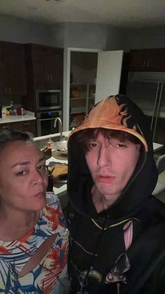 a man and woman standing in a kitchen next to each other, one wearing an orange hat