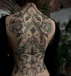 the back of a woman's body with flowers on it and an intricate design