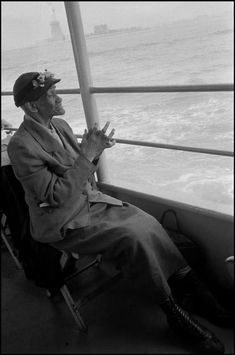 a man sitting in a chair on top of a boat near the ocean and holding his hands up