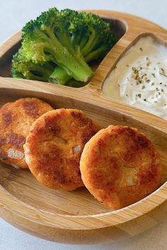 some food is on a wooden plate with dip and broccoli in the background