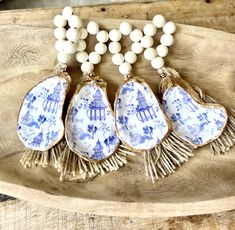 three blue and white porcelain pieces with tassels on a wooden tray next to beads