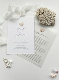 the wedding stationery is laid out on top of some pearls and seashells