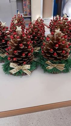 three pine cones decorated with red berries and gold bowknots are sitting on a table