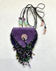 a purple purse with some beads hanging off of it's side on a white surface