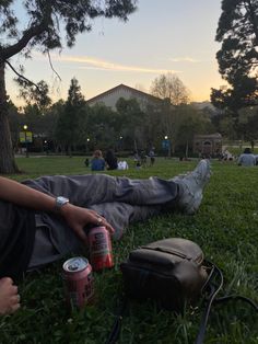 a man laying in the grass with two cans of soda and a backpack on his lap