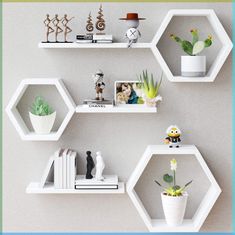 three white hexagonal shelves with plants and other items on them in front of a gray wall