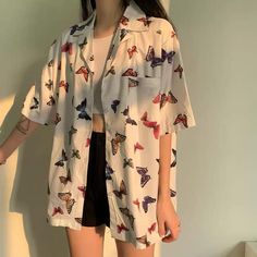 a woman standing in front of a wall wearing a white shirt with butterflies on it